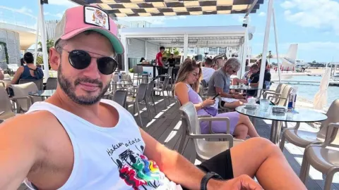 Boris Rogoznica sa sunčanim naočalama i kapom sjedi na terasi kafića uz more.