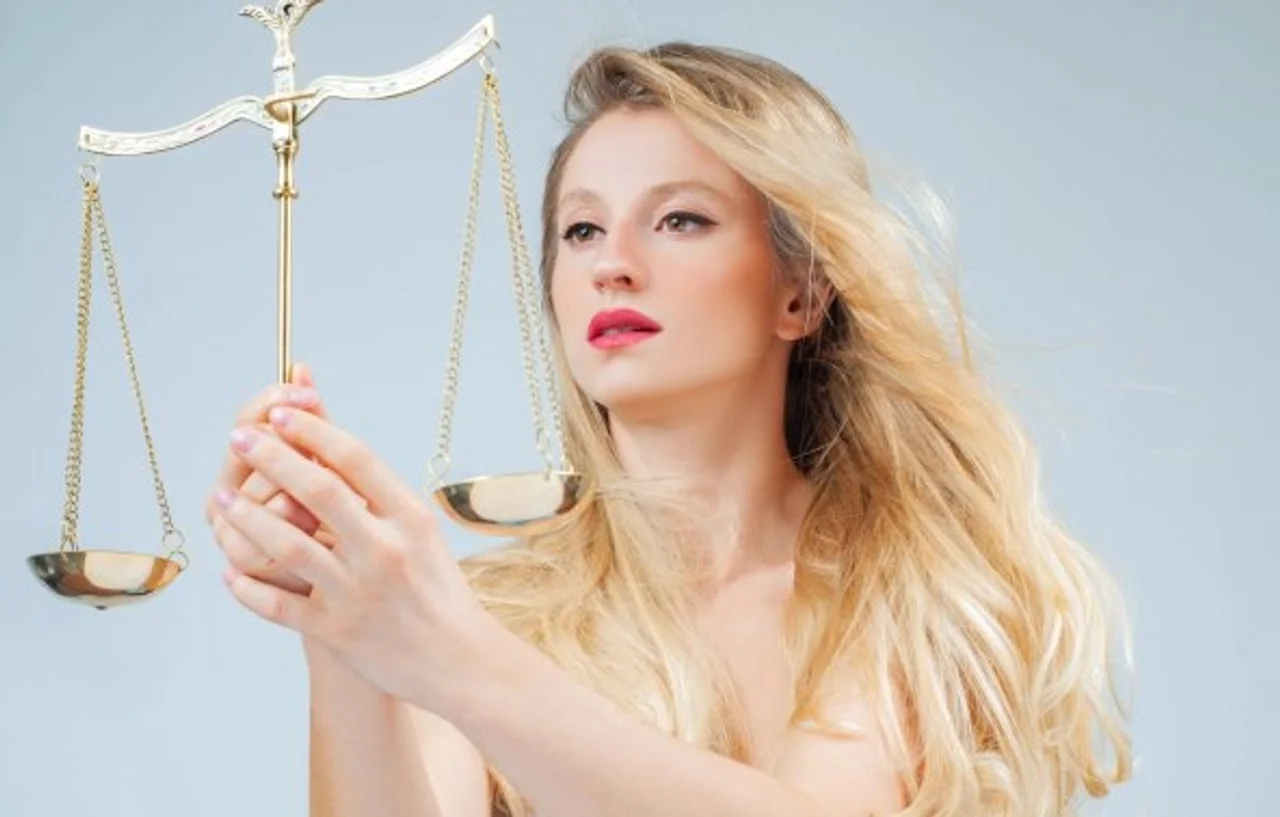 Plavokosa žena drži starinsku zlatnu vagu na sivoj pozadini