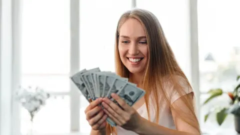 Nasmiješena žena drži lepezu novčanica američkih dolara u rukama