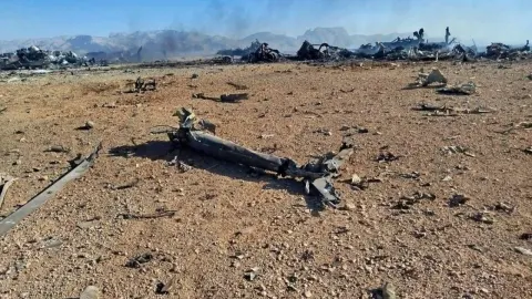 Olupine uništenih vojnih letjelica na pješčanom terenu u pustinji pod plavim nebom.