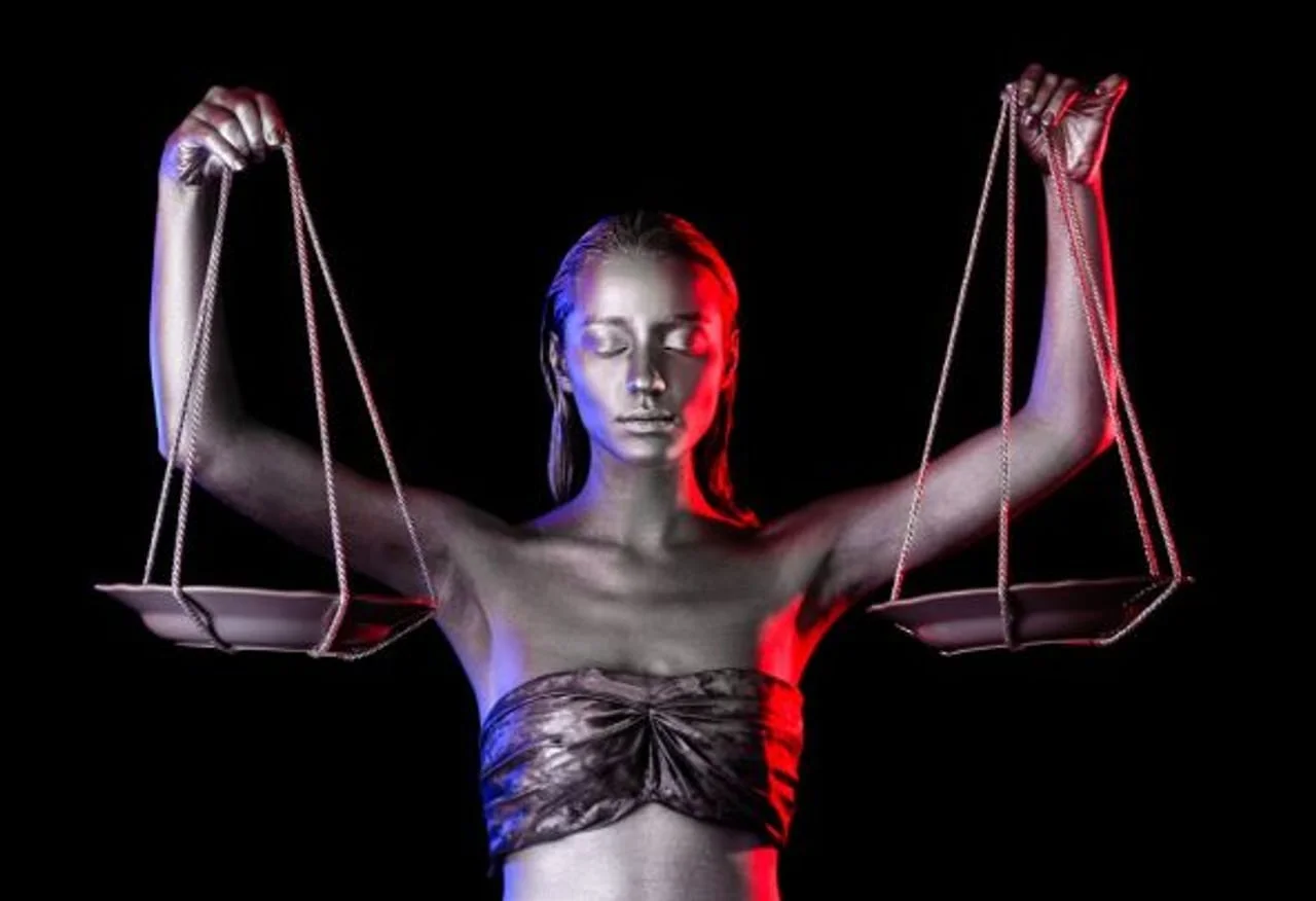 Žena srebrne kože drži vage u rukama pod crvenim i plavim svjetlom