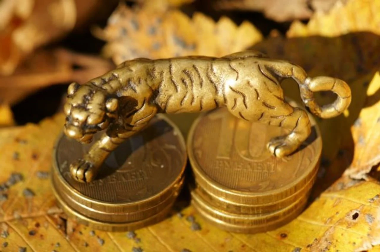 Zlatna figura tigra u skoku postavljena na hrpu kovanica