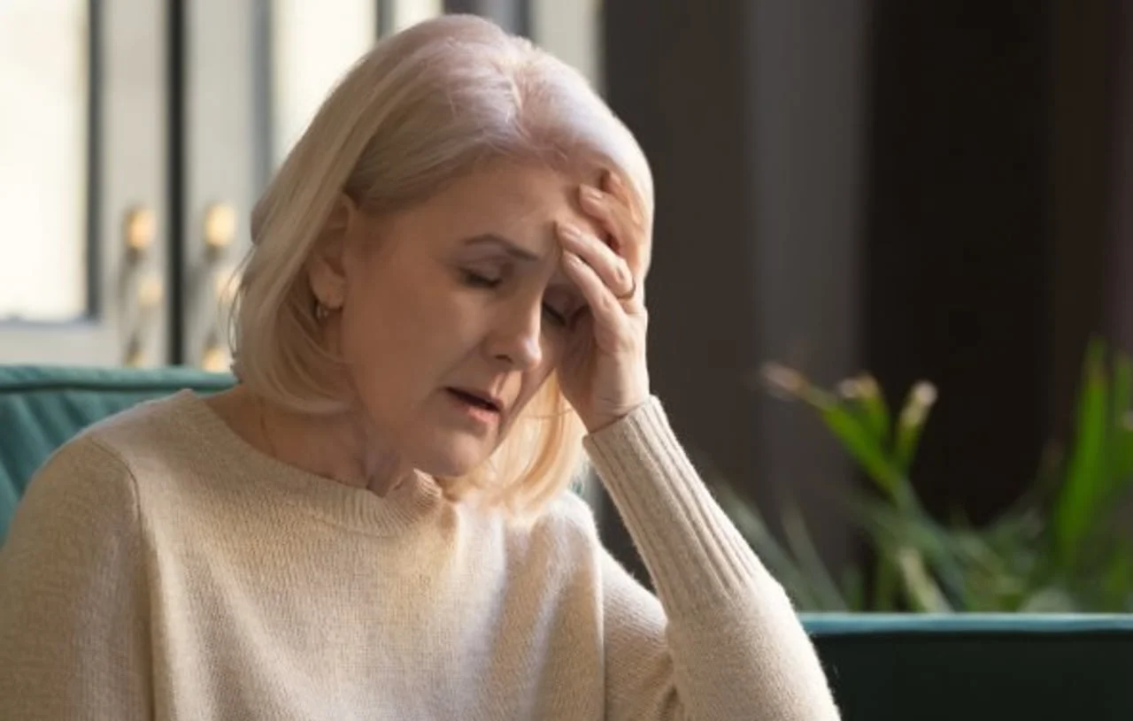 Starija žena s plavom kosom drži se za glavu s izrazom nelagode.