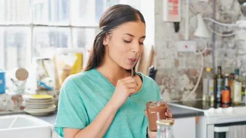 Djevojka u zelenoj majici jede čokoladni namaz iz staklenke u kuhinji.
