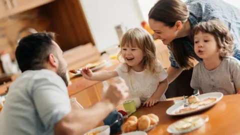 Sretna obitelj s djecom sjedi za stolom i uživa u zajedničkom obroku u kuhinji.