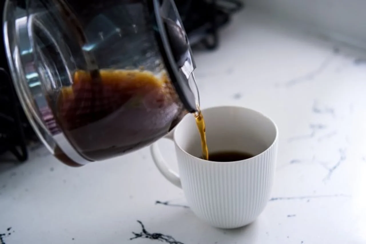 Izlijevanje crne kave iz staklenog vrča u bijelu porculansku šalicu