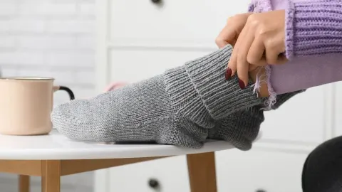 Žena oblači debele sive vunene čarape na stopala
