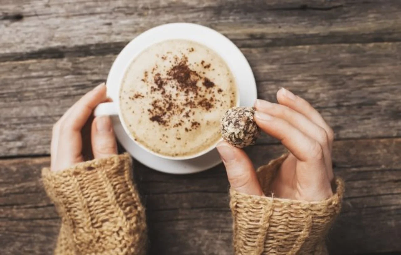 Ruke drže čokoladnu kuglicu iznad šalice kave s pjenom