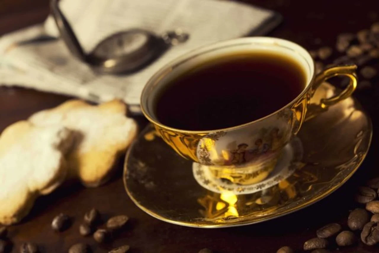 Starinska šalica crne kave na stolu uz kekse i džepni sat