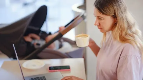 Žena pije kavu dok sjedi za stolom s prijenosnim računalom