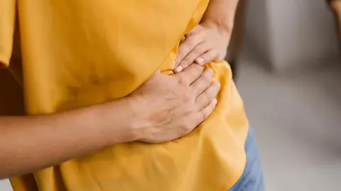 Osoba u žutoj majici drži se rukama za predjel trbuha zbog bolova.