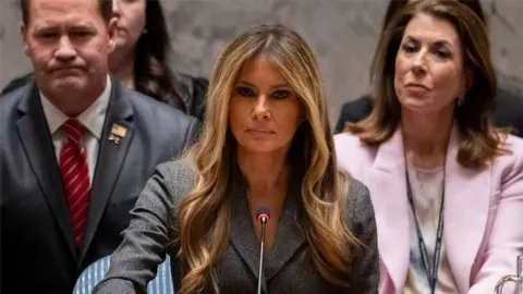 Melania Trump sjedi za govornicom UN-a u tamno sivoj jakni ispred mikrofona.