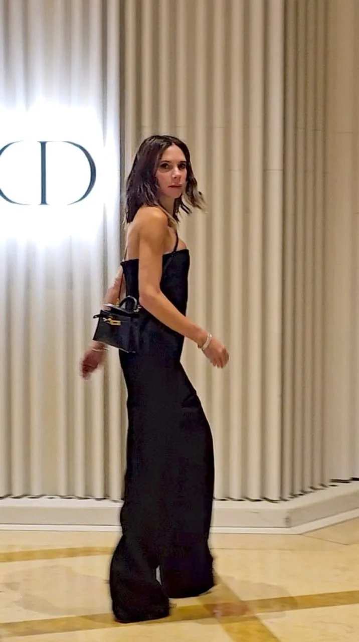 Victoria Beckham u dugoj crnoj haljini ispred logotipa Dior