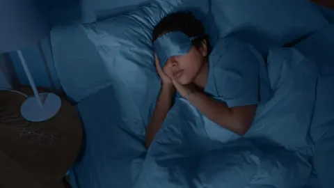 Osoba spava u krevetu s maskom za oči u tamnoj sobi
