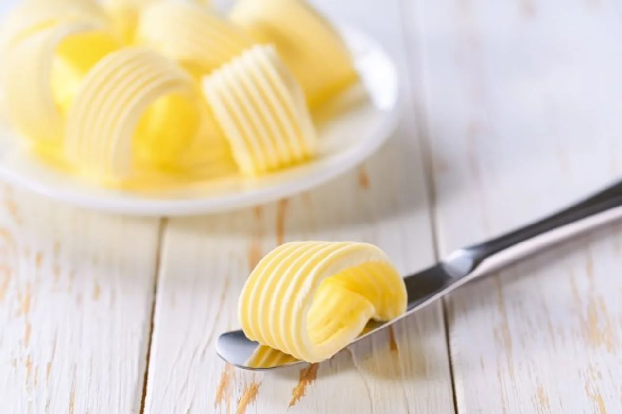 Uvojak svježeg maslaca na metalnom nožu iznad bijelog tanjura