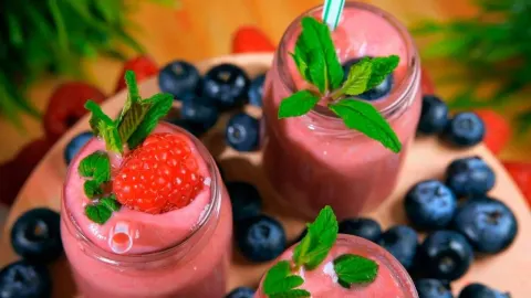 Ružičasti voćni smoothie u staklenkama ukrašen malinama i mentom