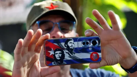 Muškarac drži pametni telefon s motivima kubanske zastave i likovima Castra i Guevare.