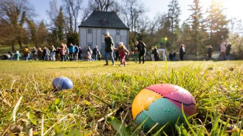 Šarena uskrsna jaja u travi s ljudima u pozadini ispred kuće.