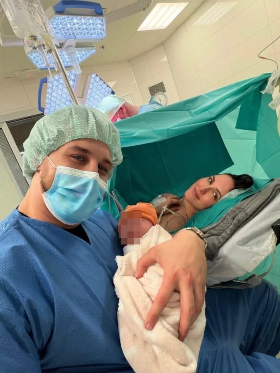 Otac drži novorođenče u naručju pored Lane Jurčević koja leži u operacijskoj sali.