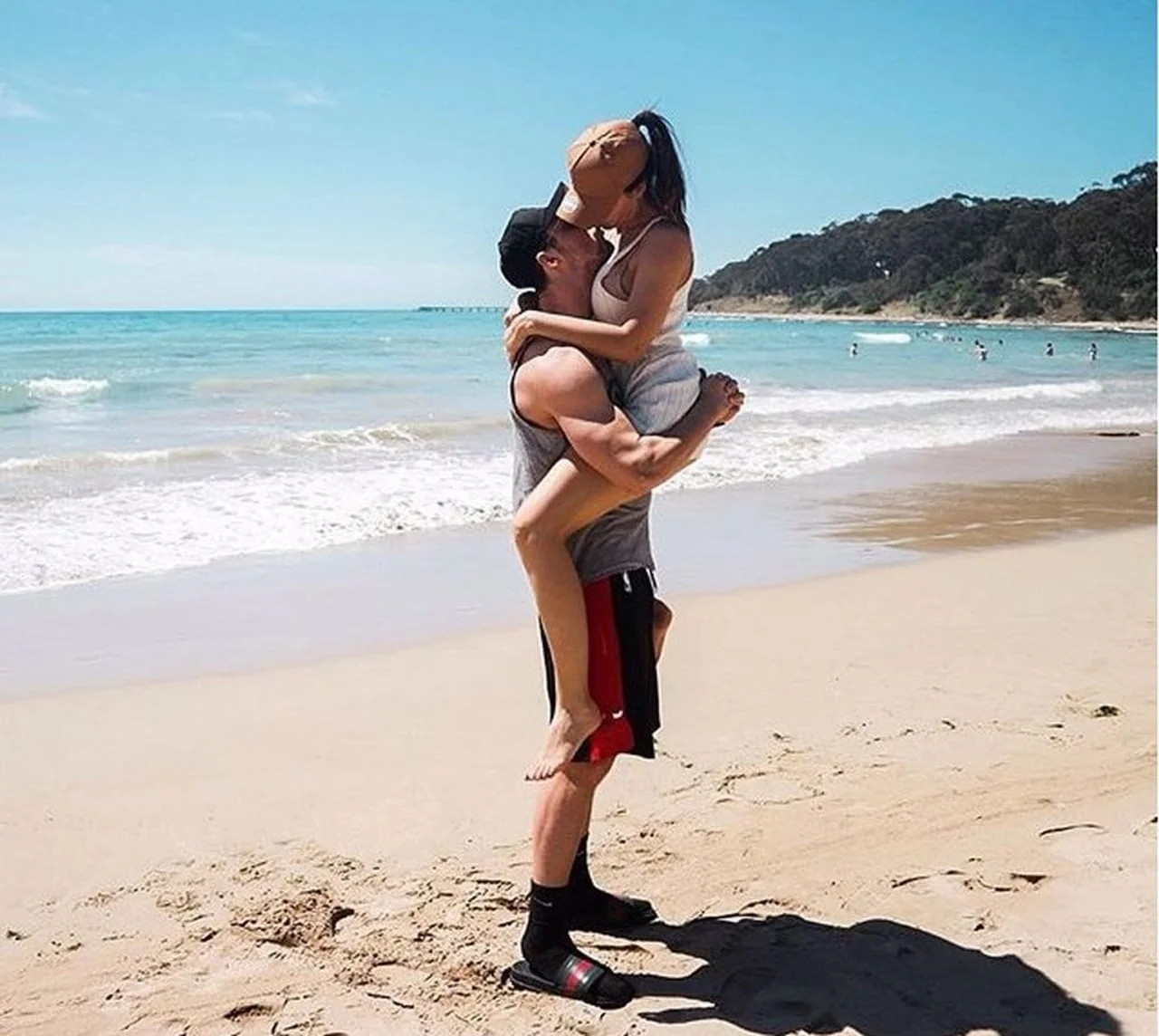 Muškarac drži ženu u naručju na pješčanoj plaži pored mora