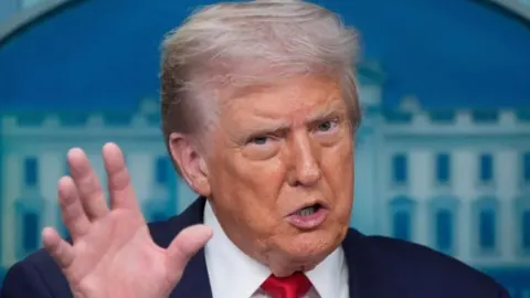 Donald Trump govori s podignutom rukom ispred plave pozadine