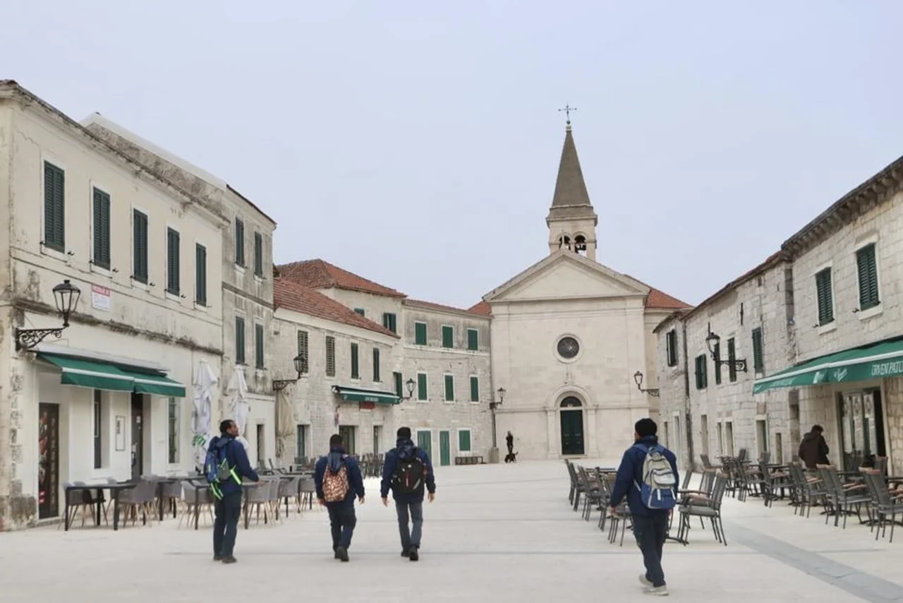 Skupina pješaka s ruksacima prelazi preko popločanog gradskog trga.