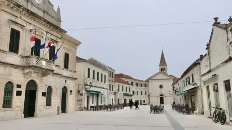 Glavni trg u Opuzenu s kamenim zgradama i crkvom u pozadini.