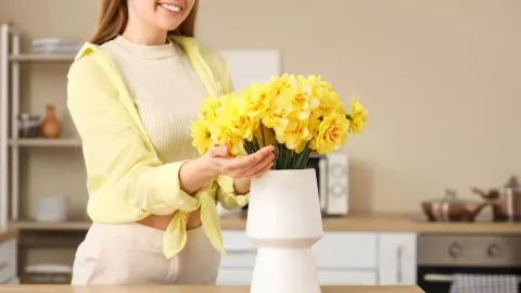 Nasmijana žena u kuhinji slaže buket žutih narcisa u bijelu vazu