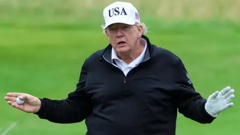 Donald Trump u crnoj jakni i bijeloj šilterici s natpisom USA na golf terenu.