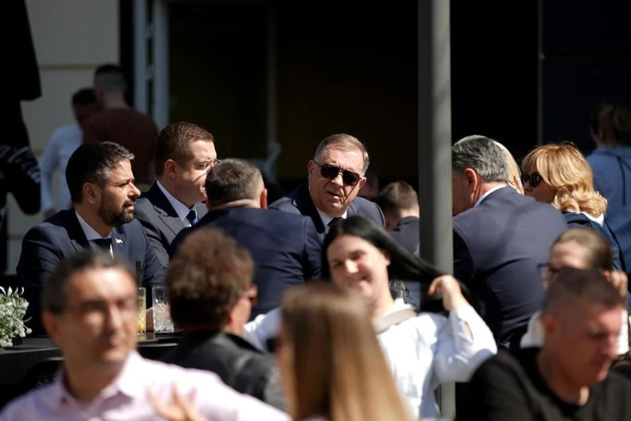 Milorad Dodik sjedi za stolom u kafiću s grupom muškaraca u odijelima.