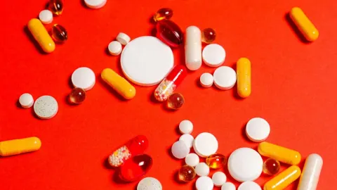 Raznobojne tablete i kapsule rasute po crvenoj podlozi.