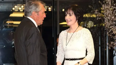 Irska pjevačica Enya u bijeloj čipkanoj haljini razgovara s muškarcem u odijelu.