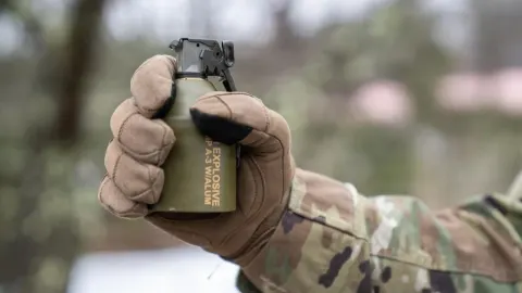 Vojnik u maskirnoj uniformi drži modernu ručnu granatu M111 u zaštitnoj rukavici.