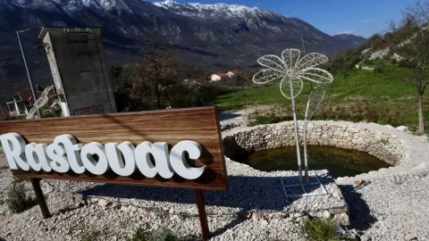 Drvena tabla s natpisom Rastovac ispred kamenog bunara i planine Biokovo