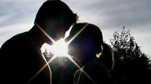 Silueta muškarca i žene okrenutih licem u lice uz efekt sunčeve svjetlosti