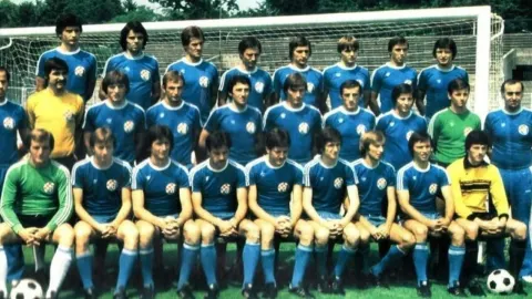 Grupna fotografija nogometaša GNK Dinamo u plavim dresovima ispred gola na stadionu.