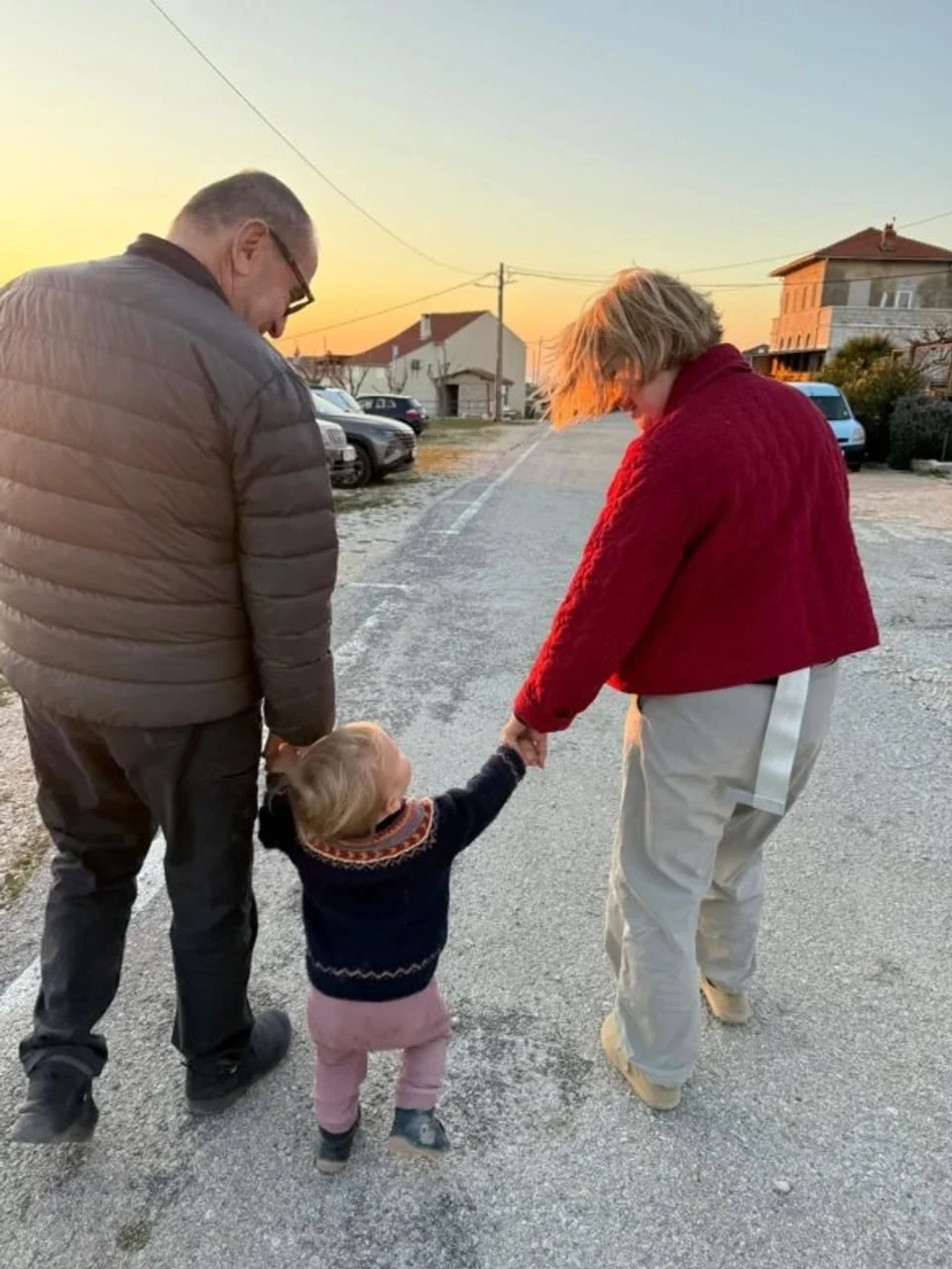 Par hoda ulicom držeći maleno dijete za ruke s leđa.