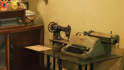 Stari radio, pisaći stroj i šivaća mašina na staklenom stolu.