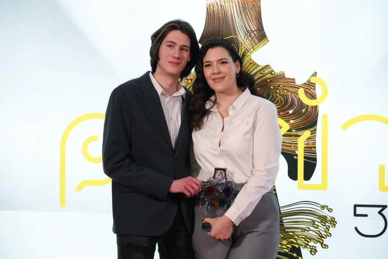 Bruno Jelusić i mlada žena poziraju s nagradom ispred brendirane pozadine