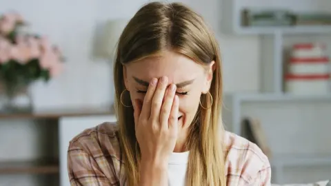 Mlada žena pokriva lice rukom u emotivnom trenutku dok sjedi u dnevnom boravku.