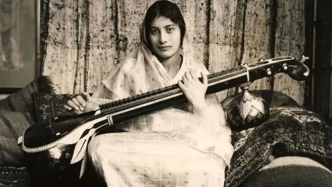 Mlada žena u tradicionalnoj odjeći drži indijski instrument veenu.