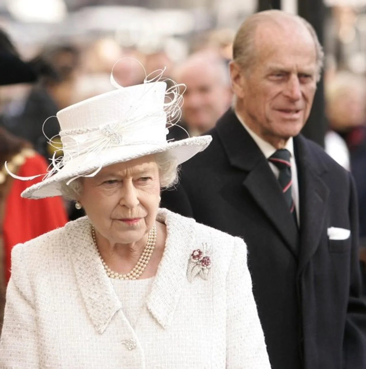 Kraljica Elizabeta II. u bijelom kostimu s princom Philipom u pozadini.