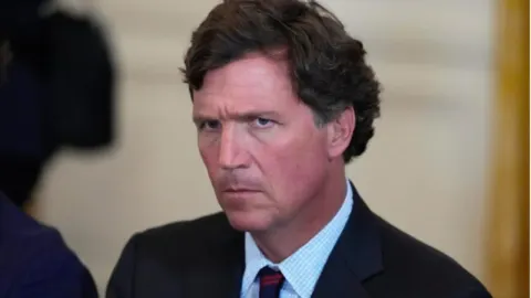 Krupni kadar Tuckera Carlsona s ozbiljnim izrazom lica u tamnom odijelu.