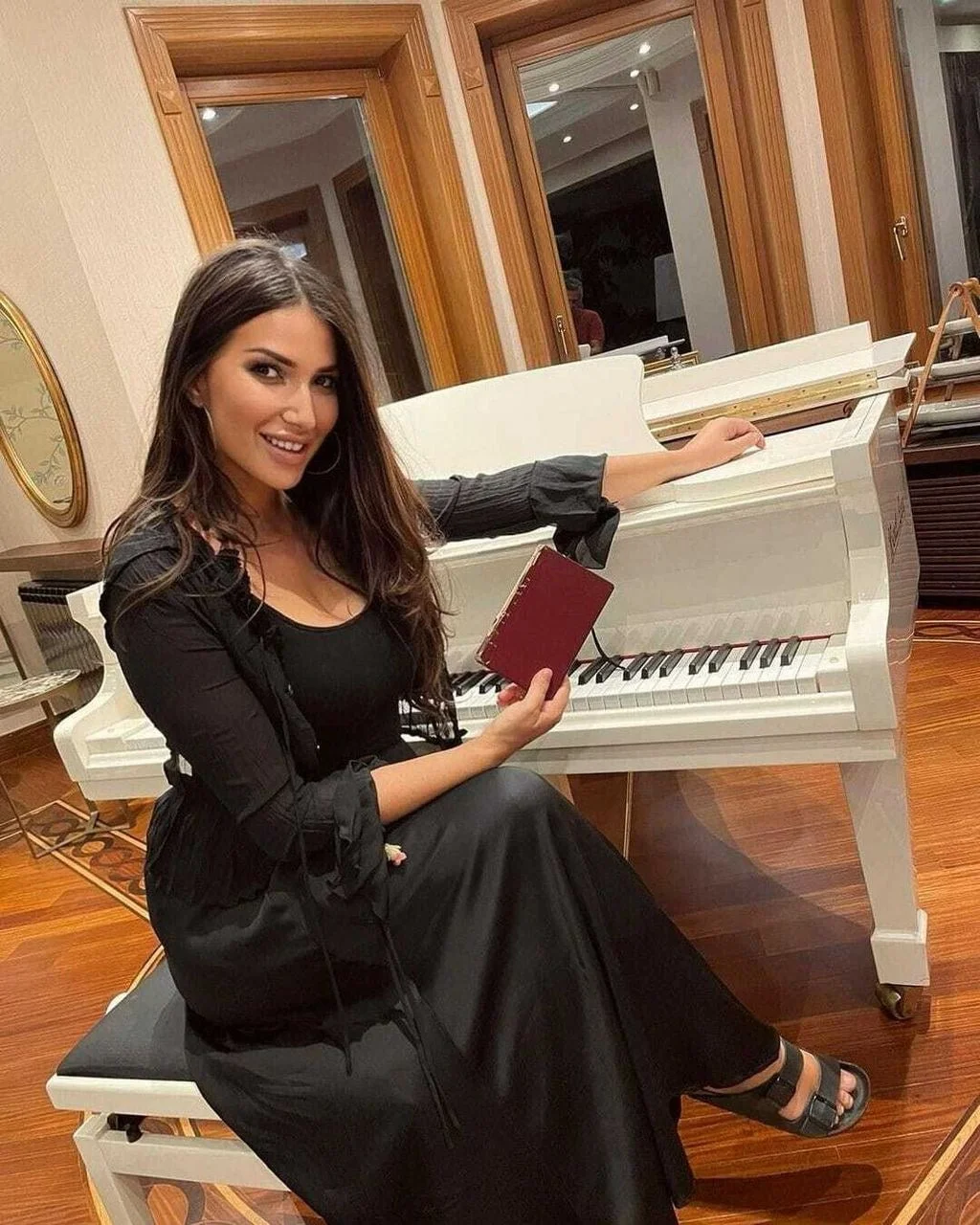 Jovana Joksimović sjedi uz bijeli klavir držeći malu knjigu