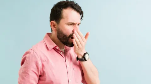 Muškarac s bradom provjerava svoj dah rukom ispred usta