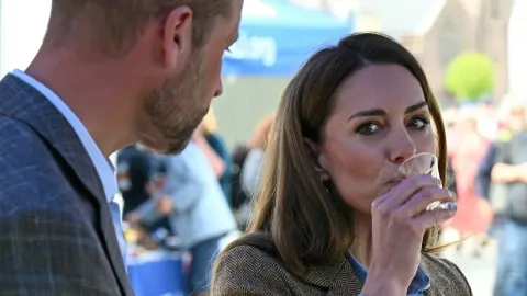 Kate Middleton pije iz male čaše dok princ William stoji pored nje.