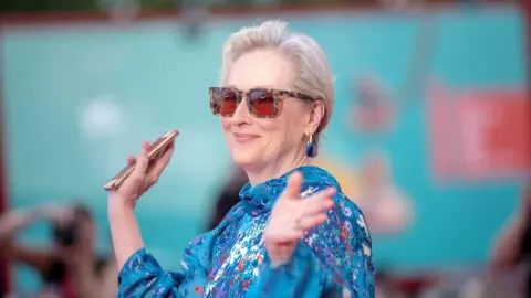 Meryl Streep s osmijehom u plavoj haljini s uzorkom i sunčanim naočalama.