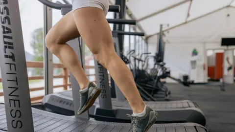 Noge trkača u pokretu na mehaničkoj traci za trčanje u teretani.