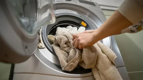 Ruke stavljaju pamučne ručnike u otvoreni bubanj perilice rublja