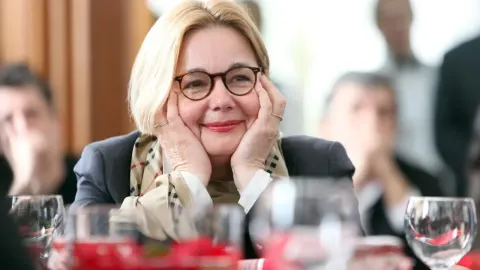 Nasmiješena Vitomira Lončar s naočalama drži lice u dlanovima za stolom.